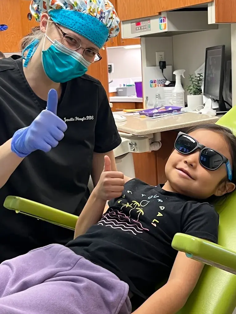 A happy young patient giving a thumbs up next to her pediatric dentist